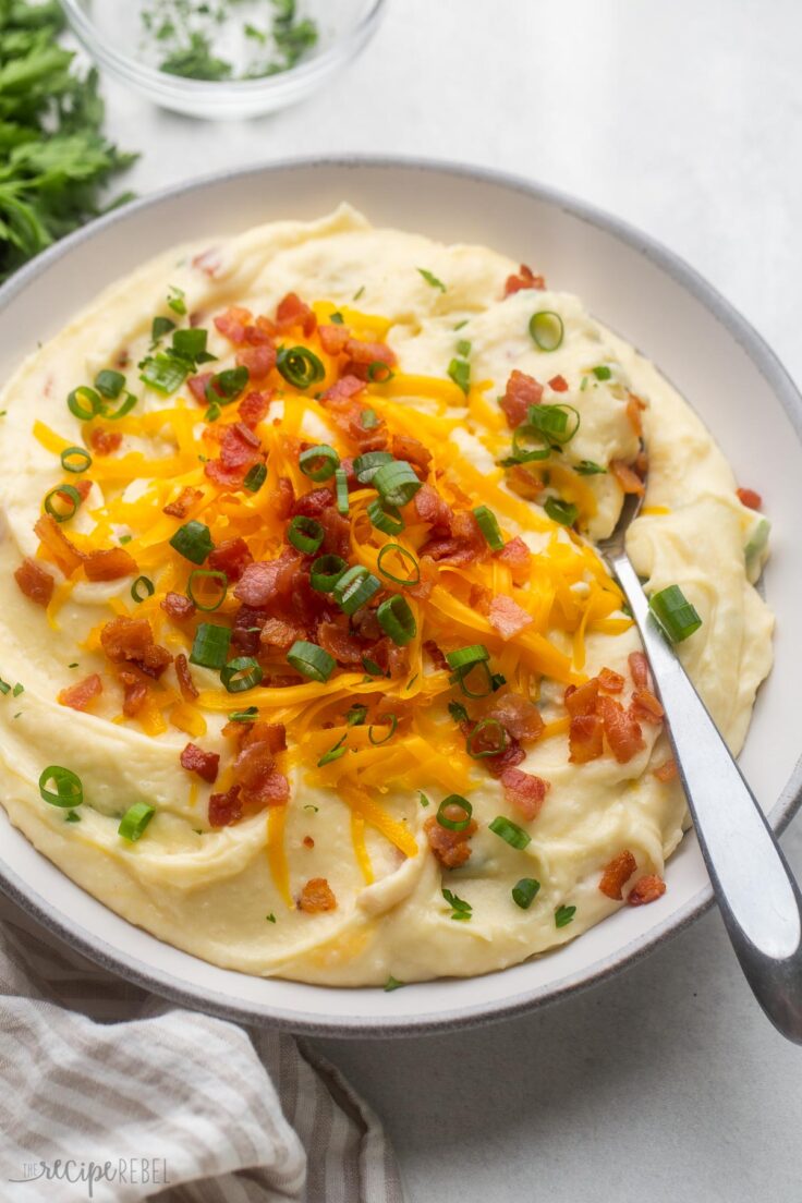 a full bowl of loaded mashed potatoes on a grey surface with parsley beside.