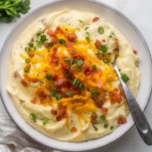 overhead of a bowl of mashed potatoes topped with cheese, green onions, and bacon bits.