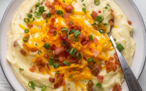 overhead of a bowl of mashed potatoes topped with cheese, green onions, and bacon bits.