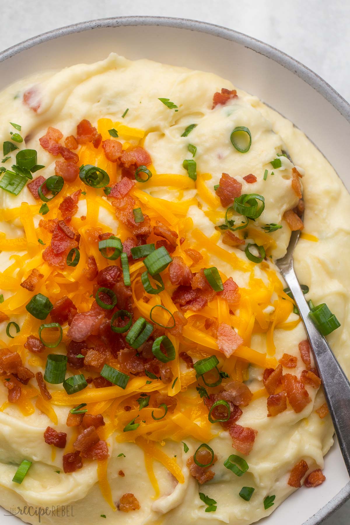 close up of a bowl of loaded mashed potatoes with a spoon in.