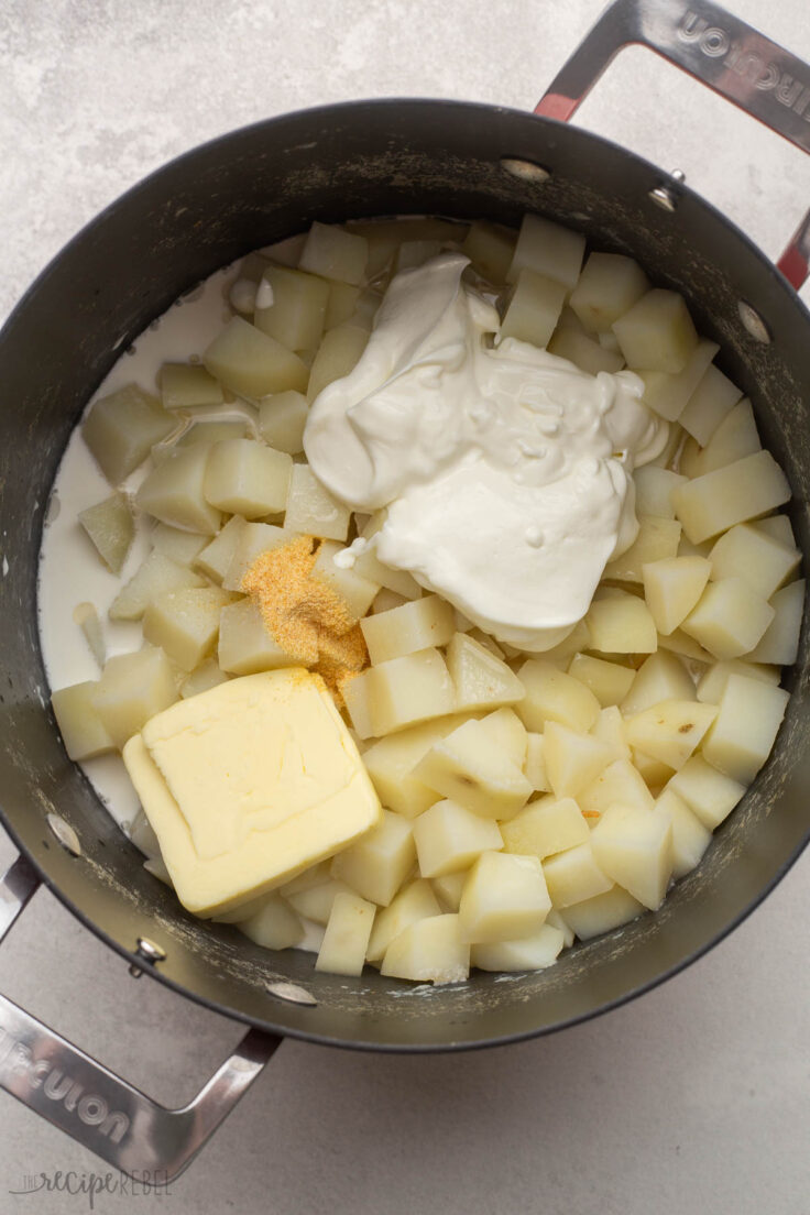 big pot of cooked potatoes with sour cream, garlic powder, and butter added on top.