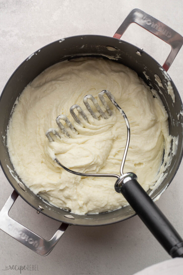 big pot of mashed potatoes with masher in pot.