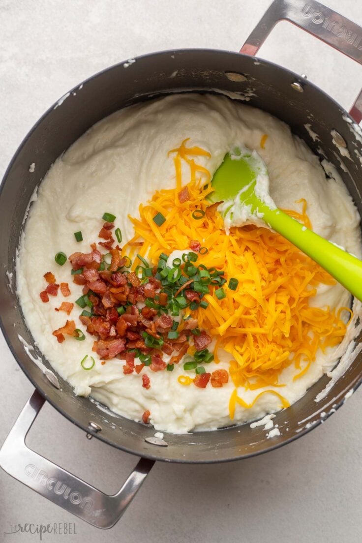 black pot of mashed potatoes with cheese, green onions, and bacon added on top.