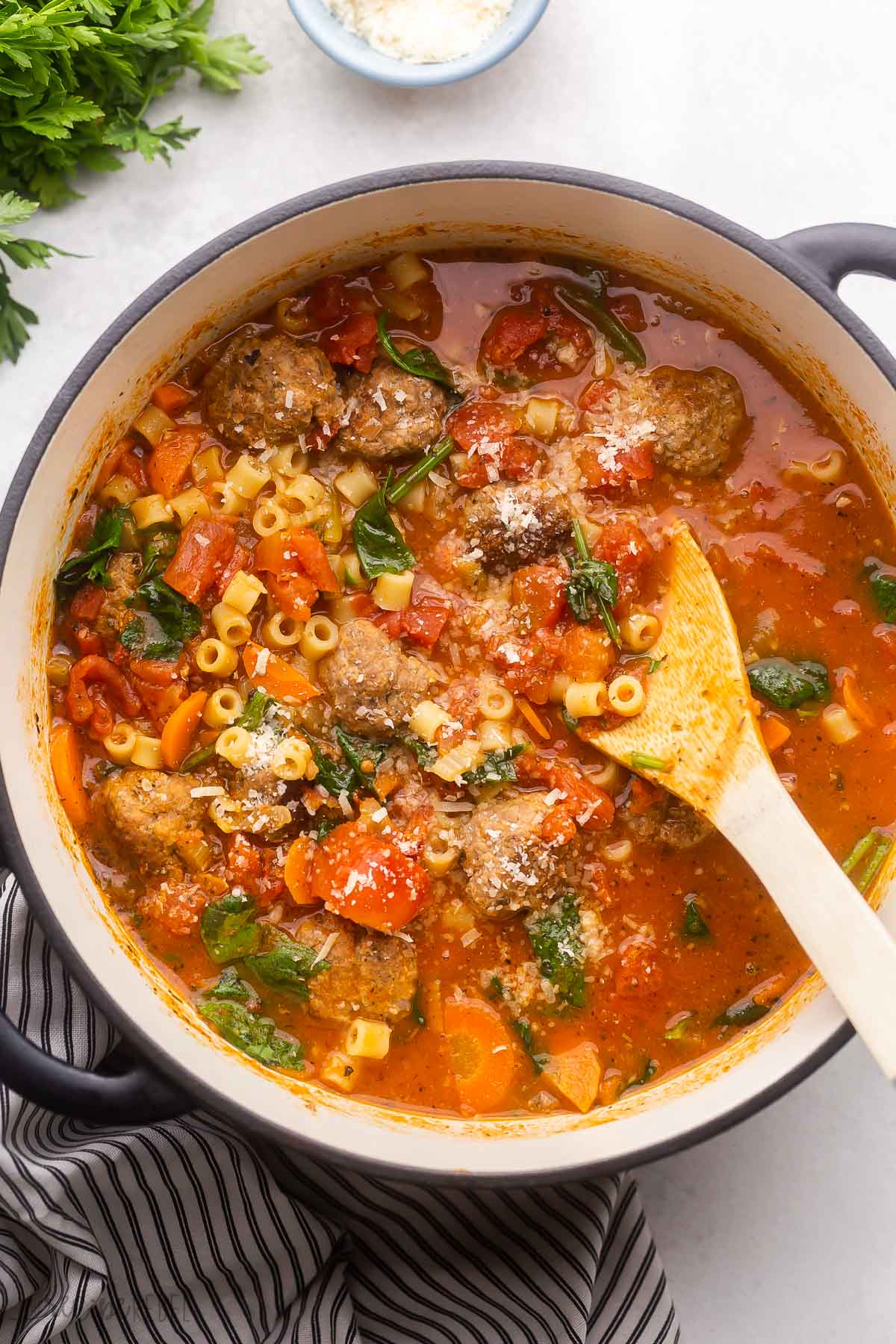 overhead view of a full pot of meatball soup with wooden ladle in it.