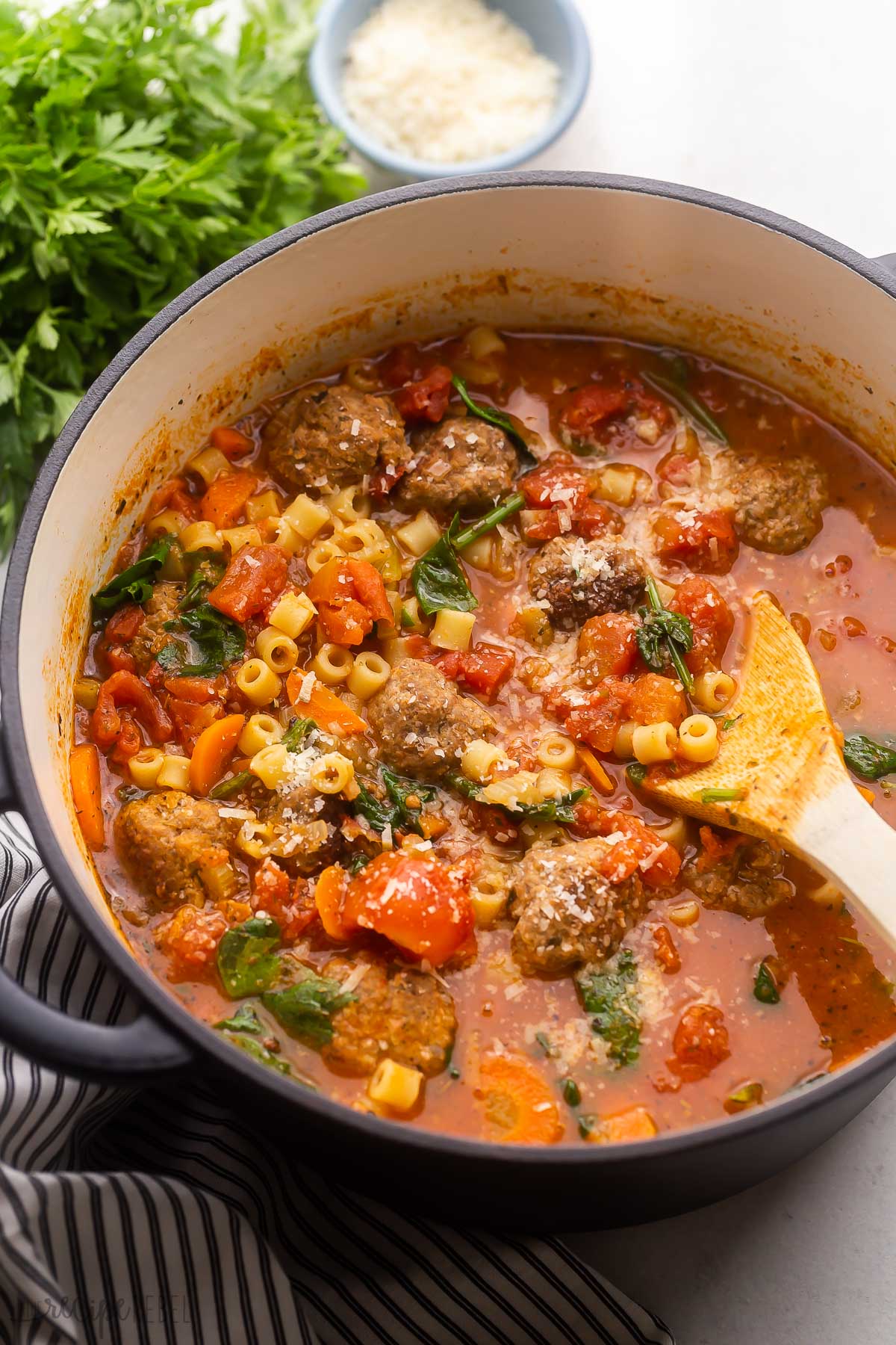 large pot of meatball soup with wooden ladle in it and fresh parsley behind it.