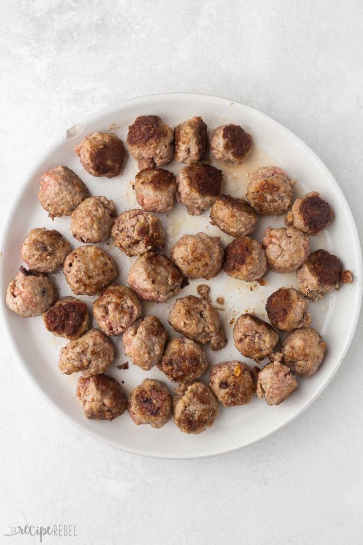 white plate full of cooked meatballs on grey surface.