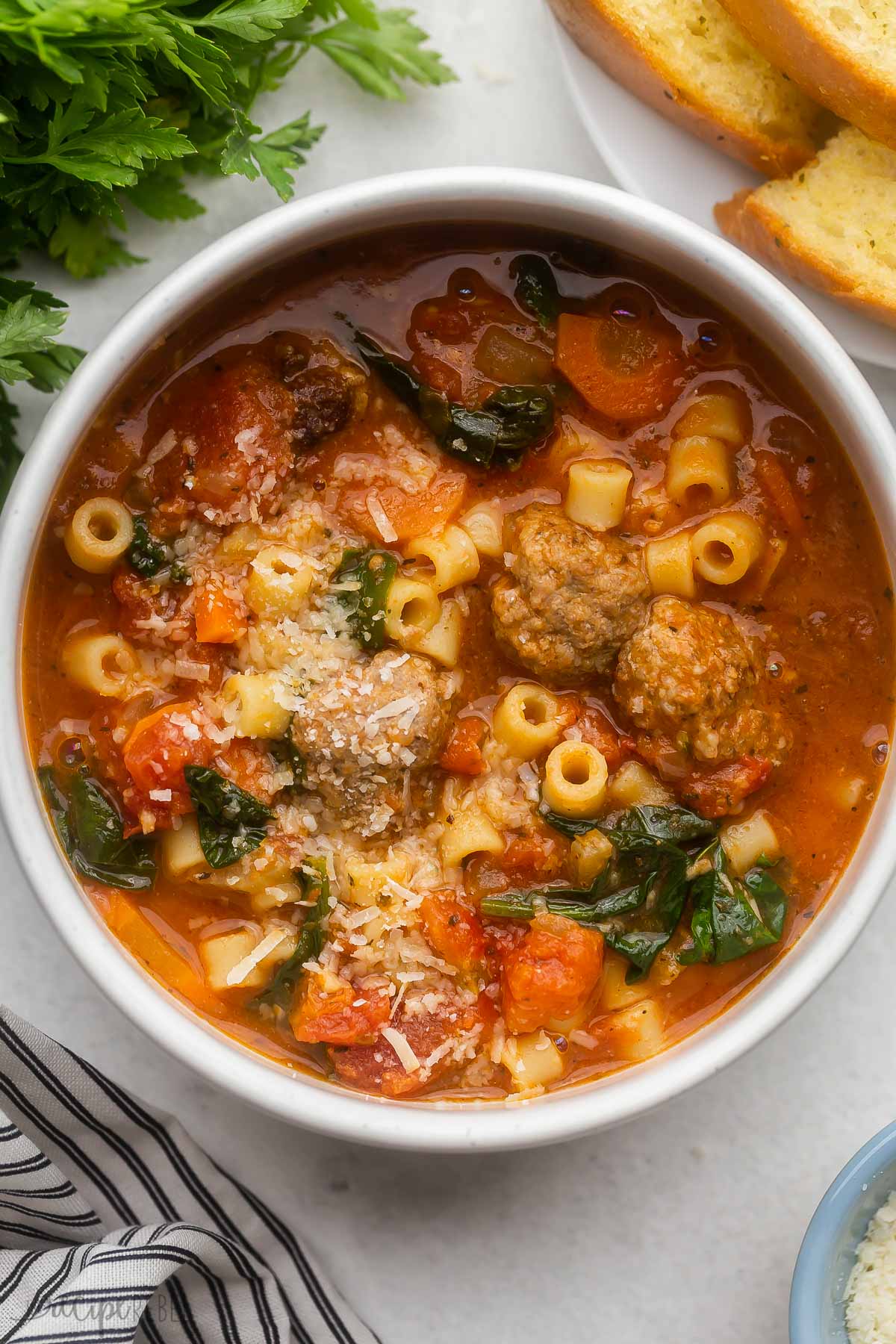 white bowl filled with meatball soup and grated parmesan cheese on top.