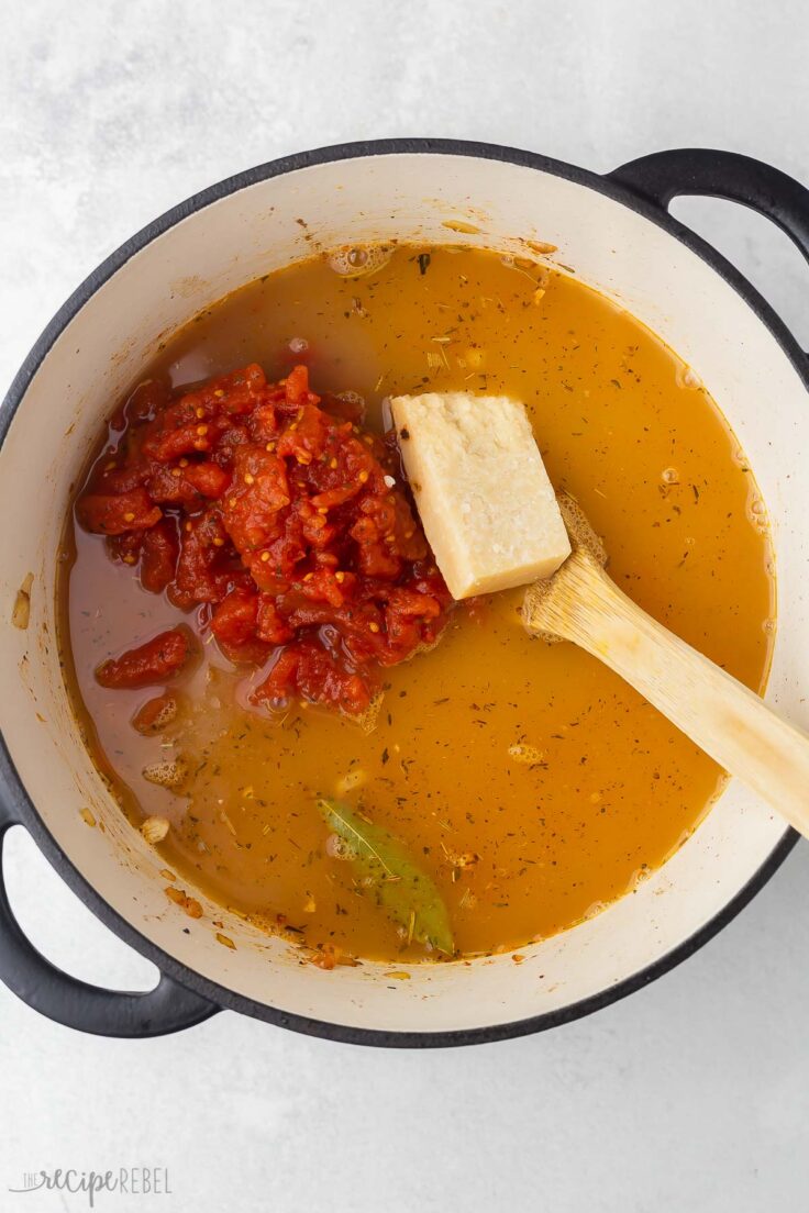 large pot filled with broth, tomatoes, parmesan rind and wooden ladle.