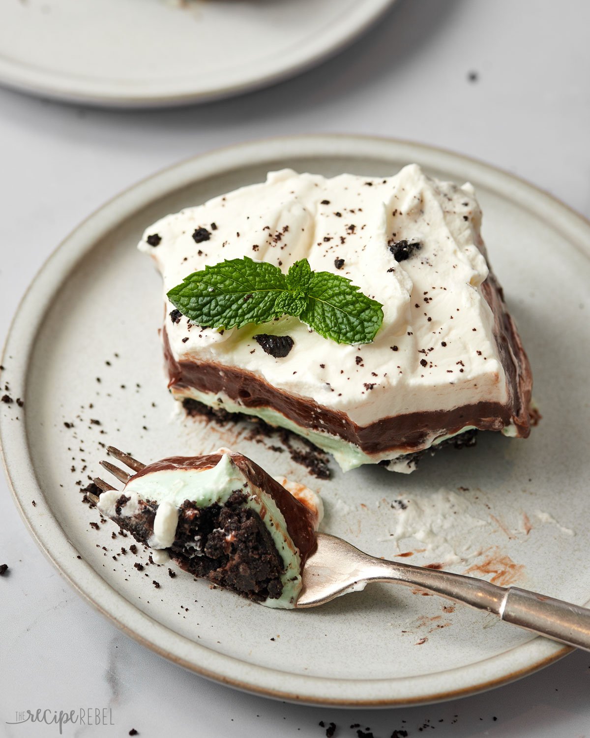 a fork full of mint chocolate lasagna beside a piece that's topped with mint leaves.