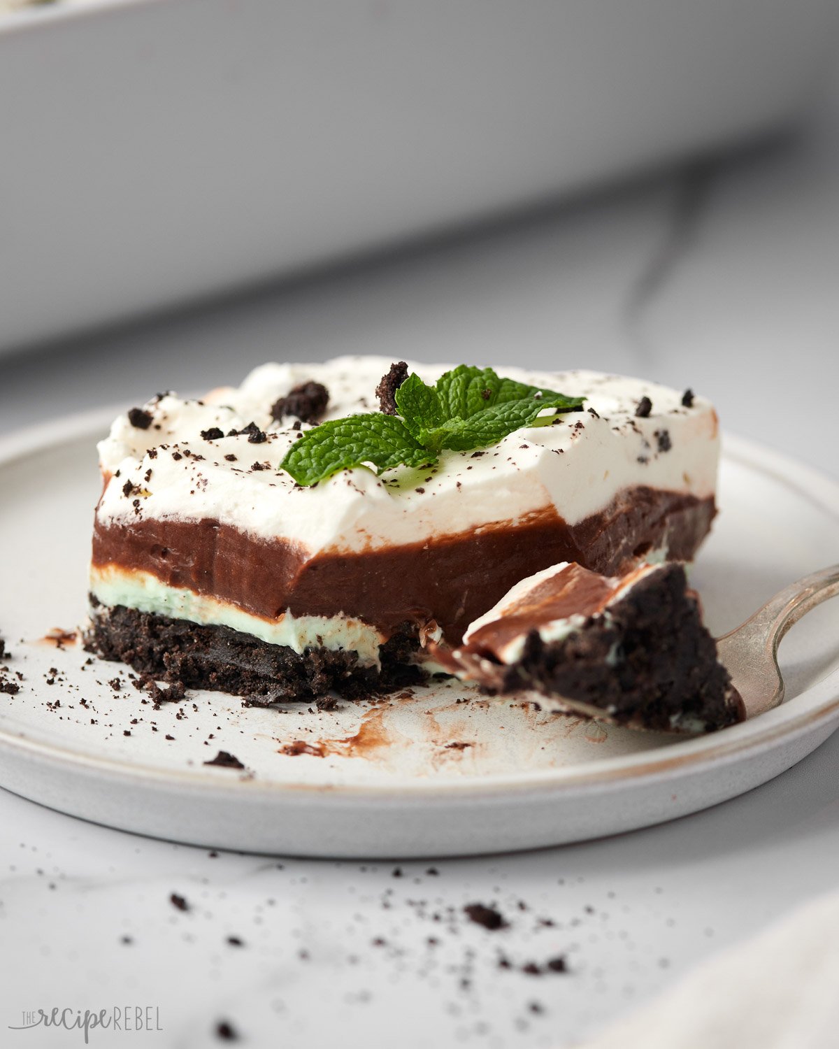 piece of chocolate mint lasagna on a white plate with a fork full beside.