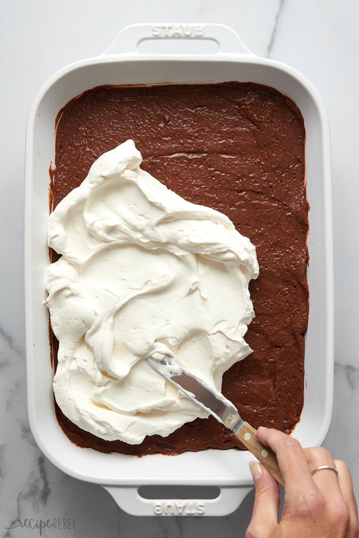 white pan with whipped cream being spread over chocolate layer.