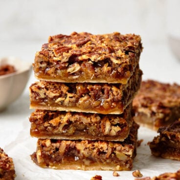 A stack of four pecan pie bars on a white surface.