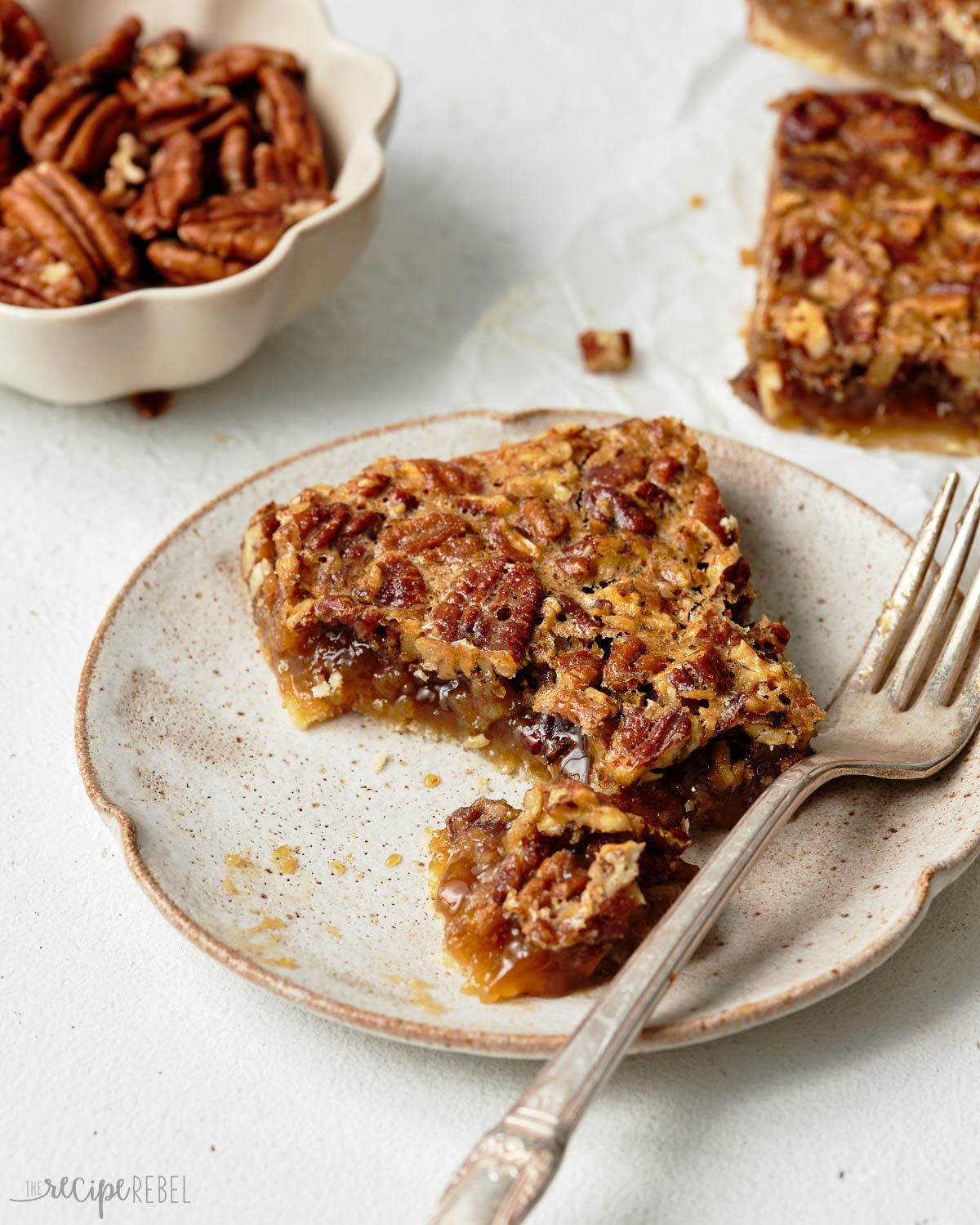 Close up of a plate with a pecan pie bar and a fork on it.