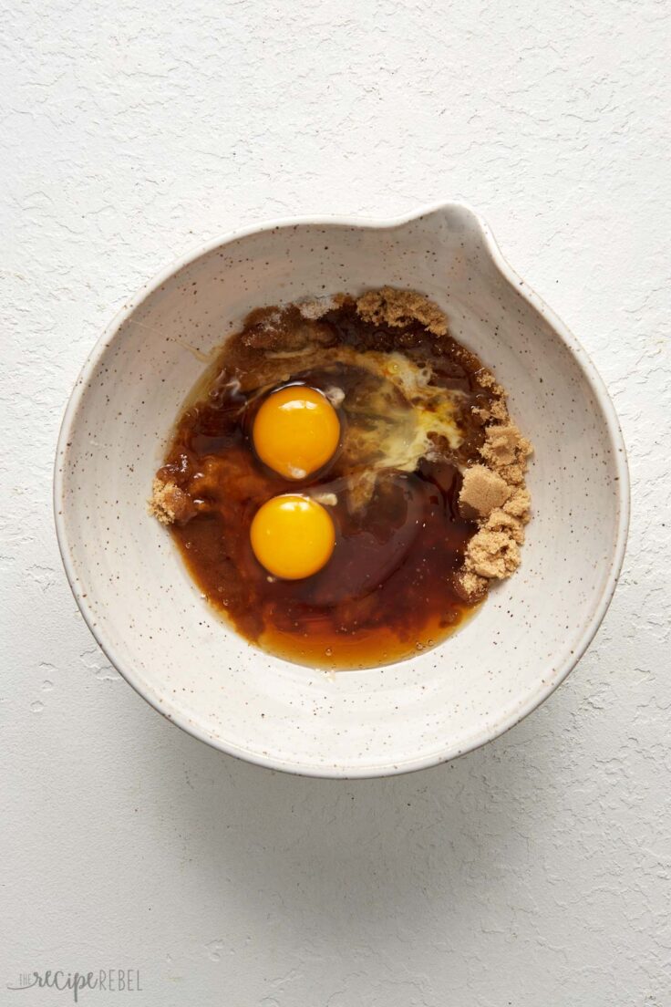 Top view of a white mixing bowl with sugars and eggs in it.