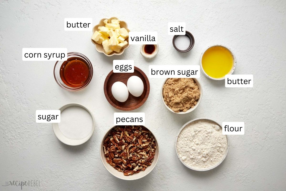 Top view of ingredients needed for pecan pie bars in small bowls on a white work top.