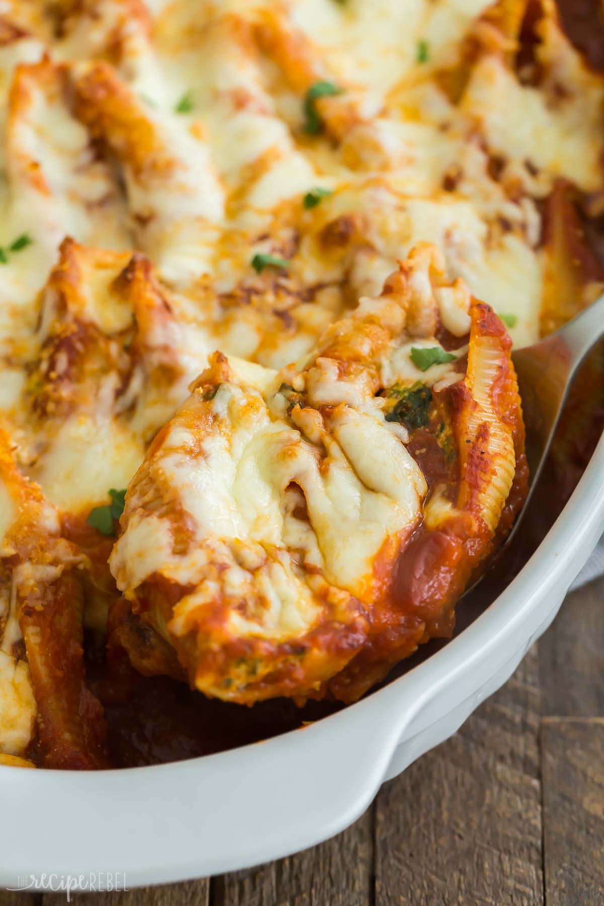 spoon scooping two stuffed shells from baking dish.