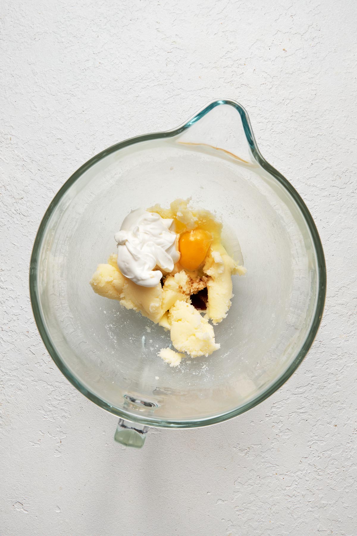 Top view of a glas mixing bowl with butter, sugar, eggs, vanilla extract, almond extract, and sour cream in it.