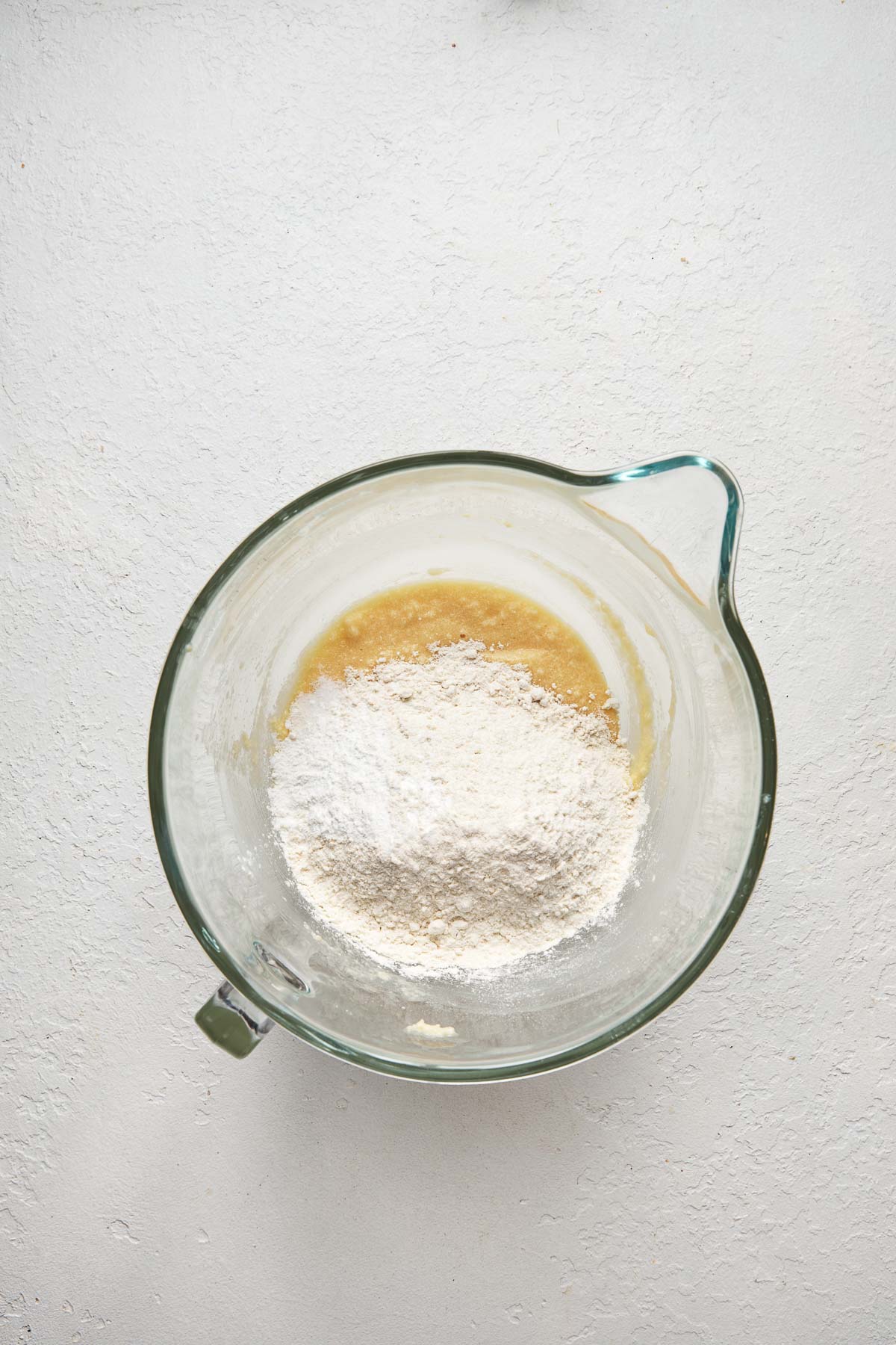 Top view of a glass mixing bowl with a creamed mixture in the bottom and flour on top.