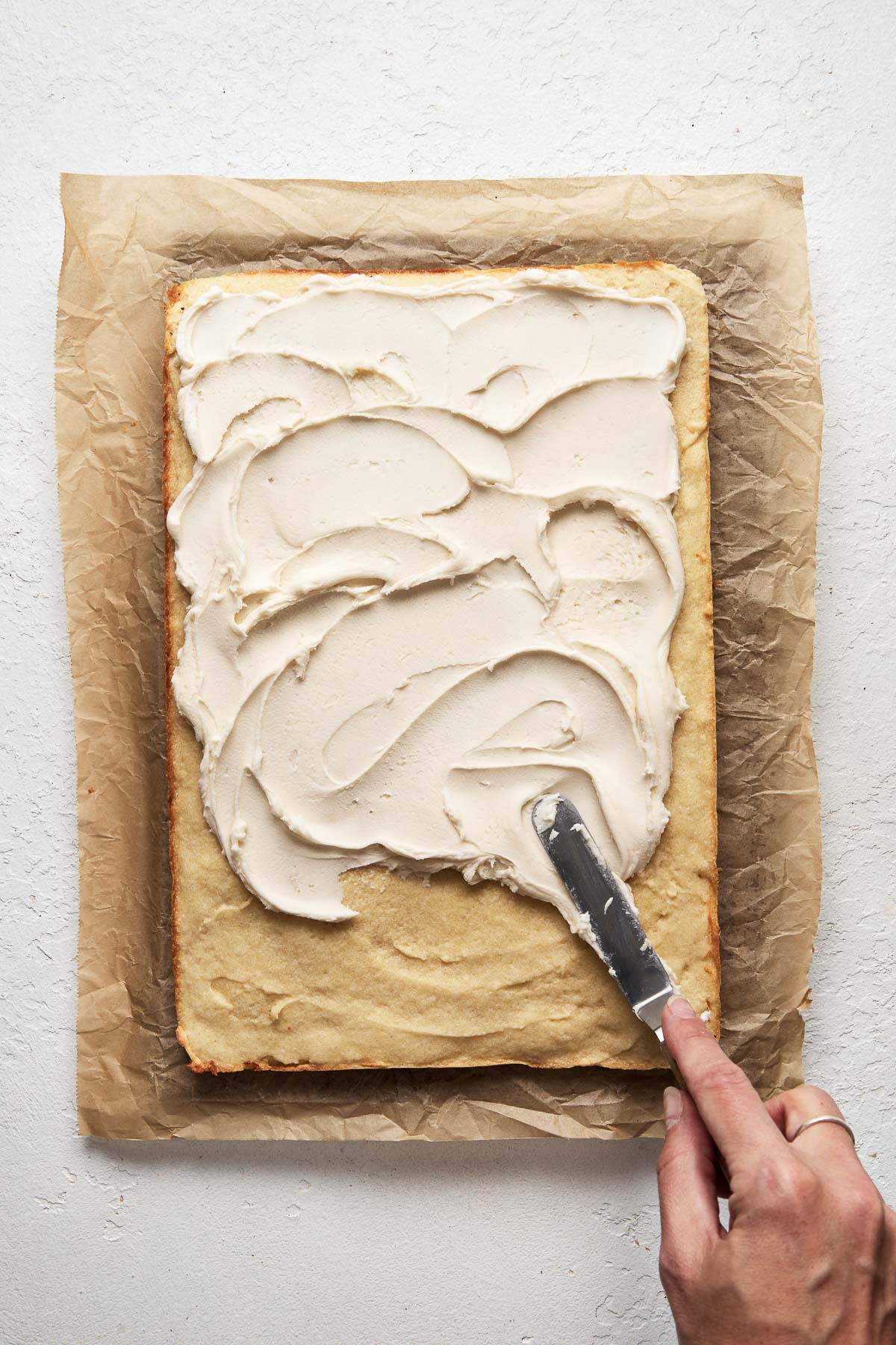 Top view of a baking pan with a cookie bar in the borrom, and a knife spreading frosting over the top.