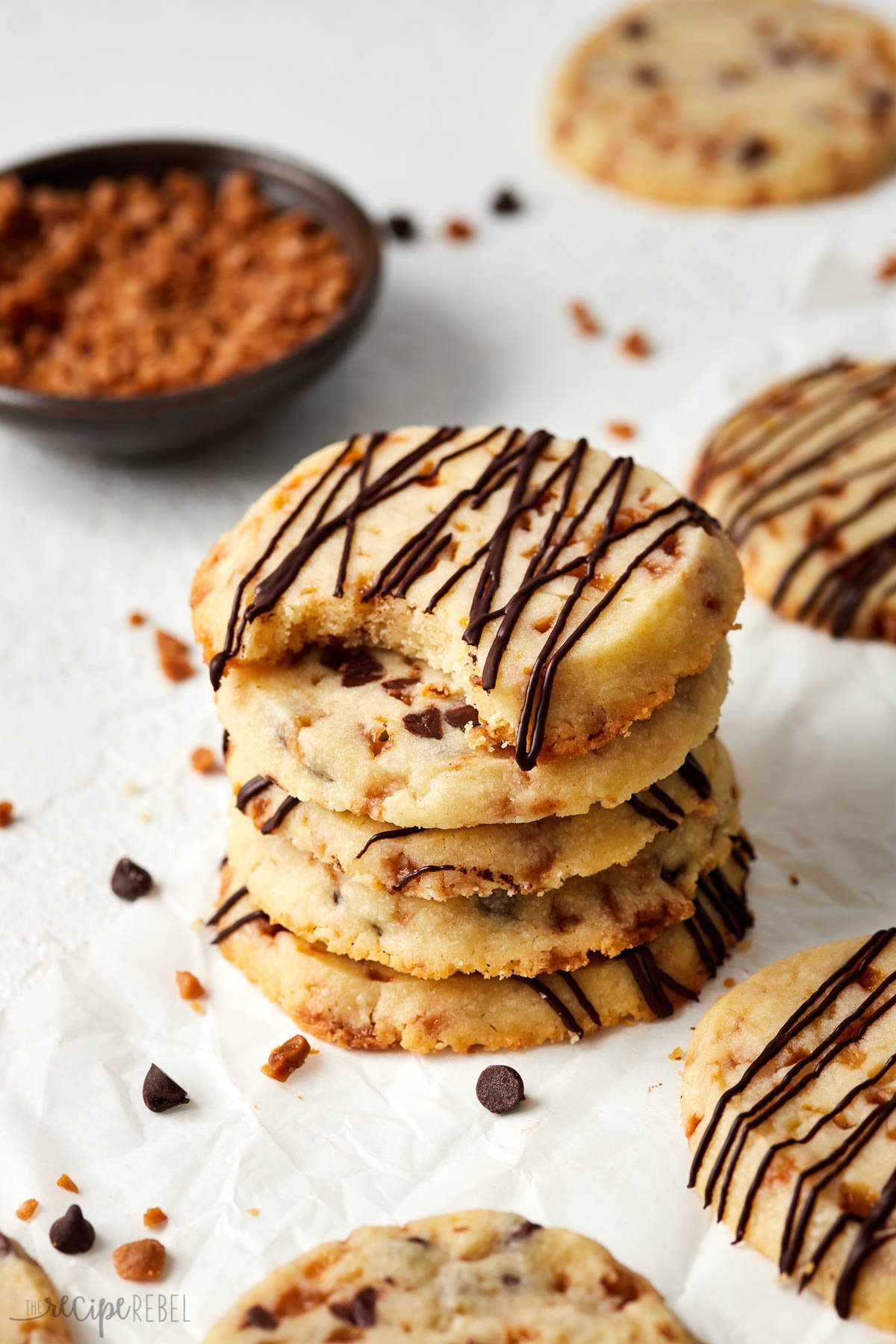 stack of cookies on parchment paper with toffee bits around.