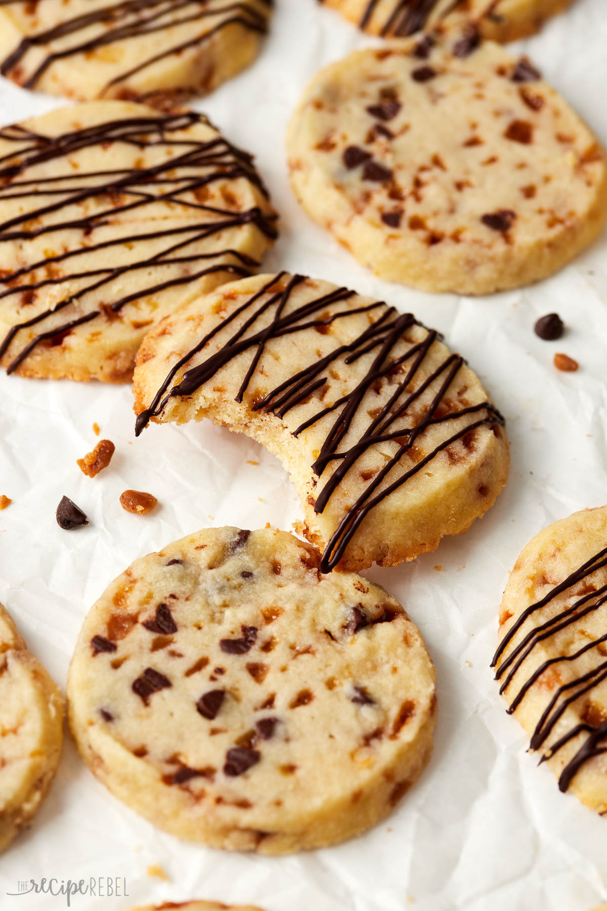 close up of a toffee shortbread cookie on parchment paper with a bite taken out of it.