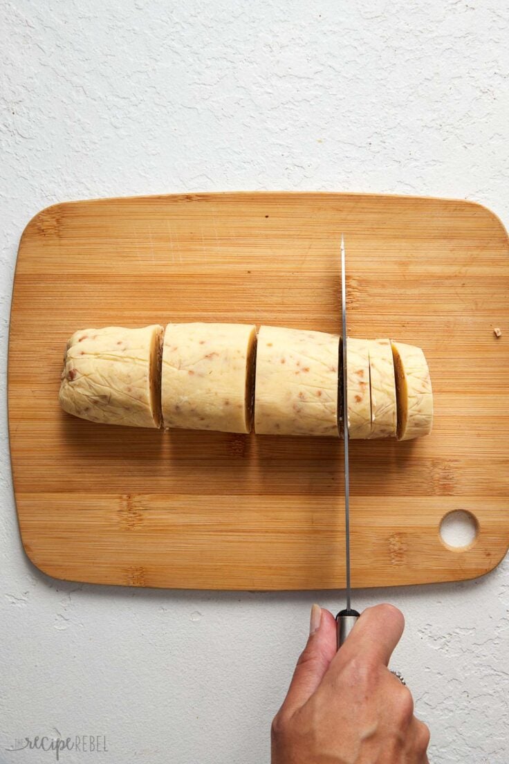 toffee shortbread roll being sliced on wooden cutting board.