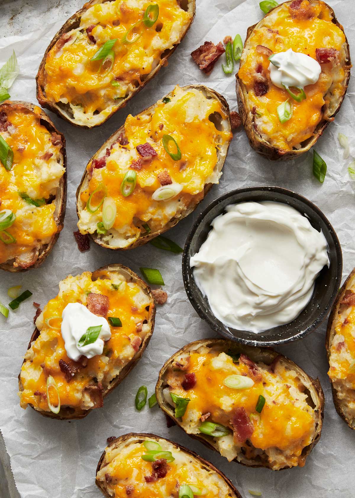 Top view of twice baked potatoes on a white plate with a small bowl of dip next to them.