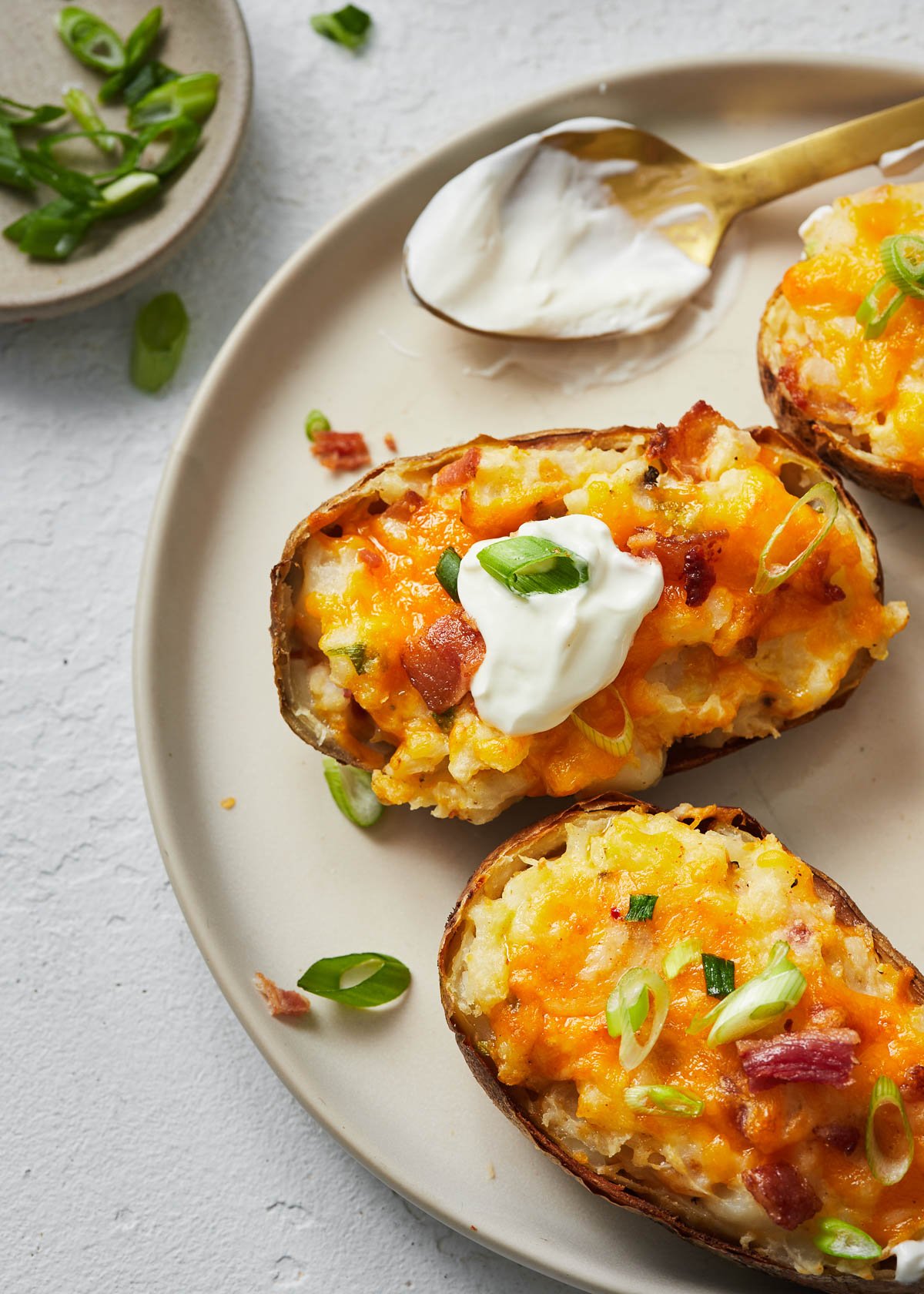 Top view of twice baked potatoes on a white plate with a dollop of dip on one.