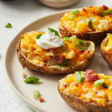 Close up of twice baked potatoes on a white plate with a dollop of dip on one.