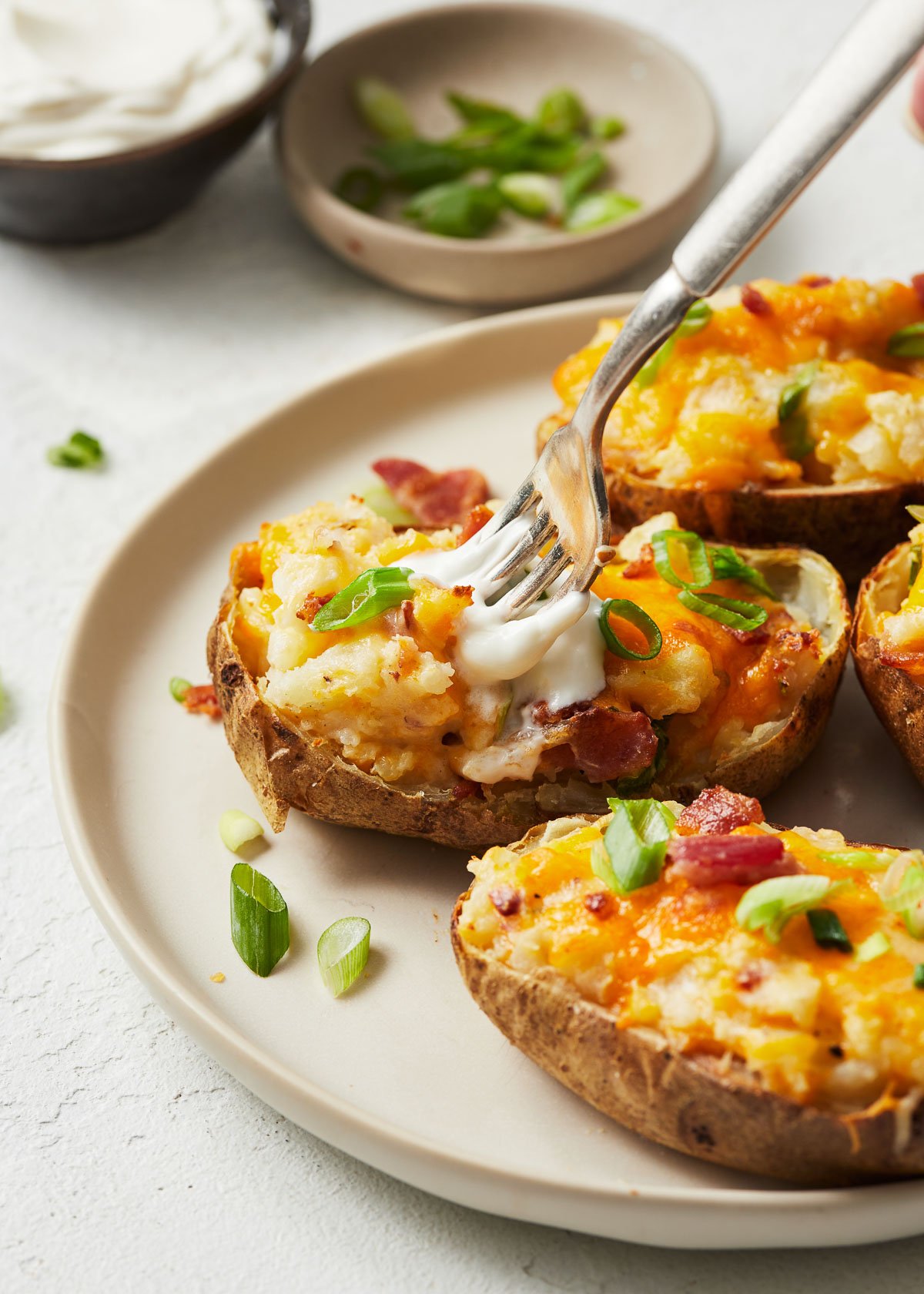 Close up of twice baked potatoes on a white plate with a dollop of dip on one and a fork sunk into it.