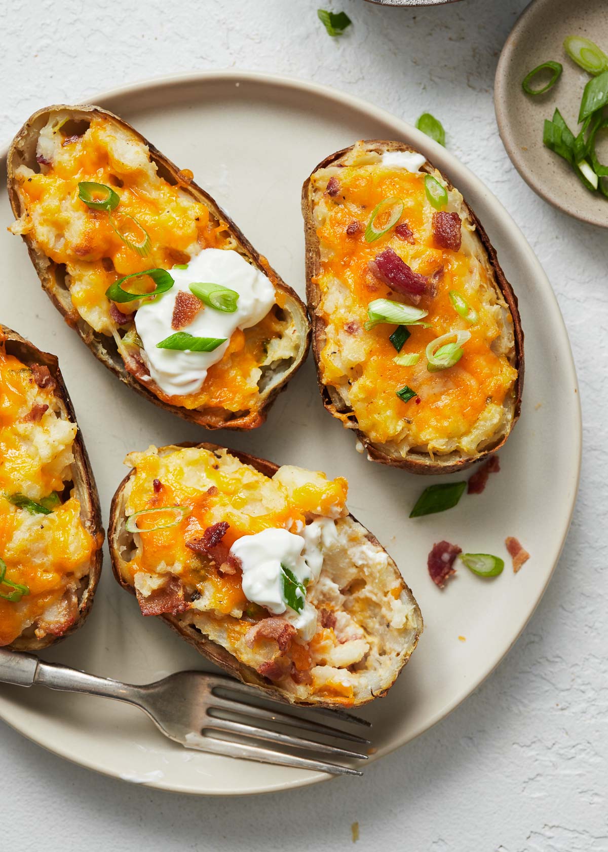 Top view of twice baked potatoes on a white plate with dollops of dip on them.