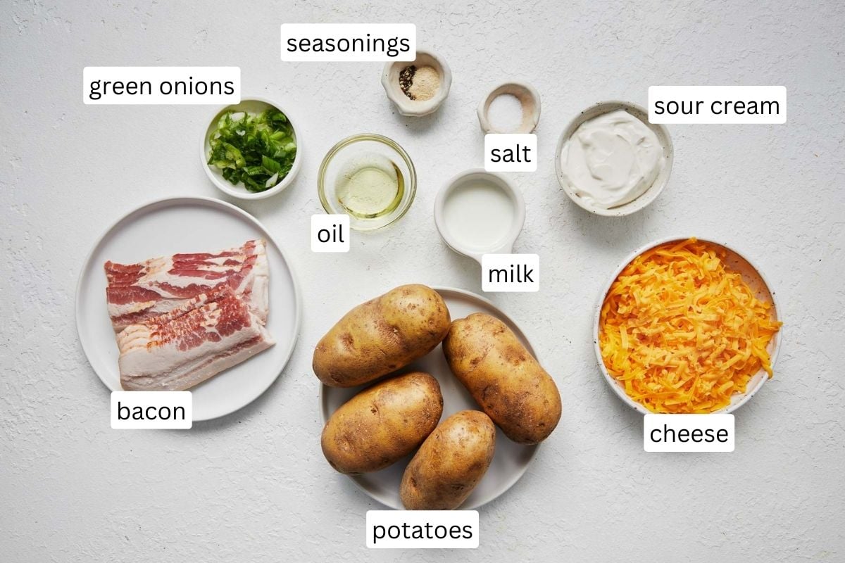 Top view of ingredients needed to make twice baked potatoes in small bowls on a white surface.