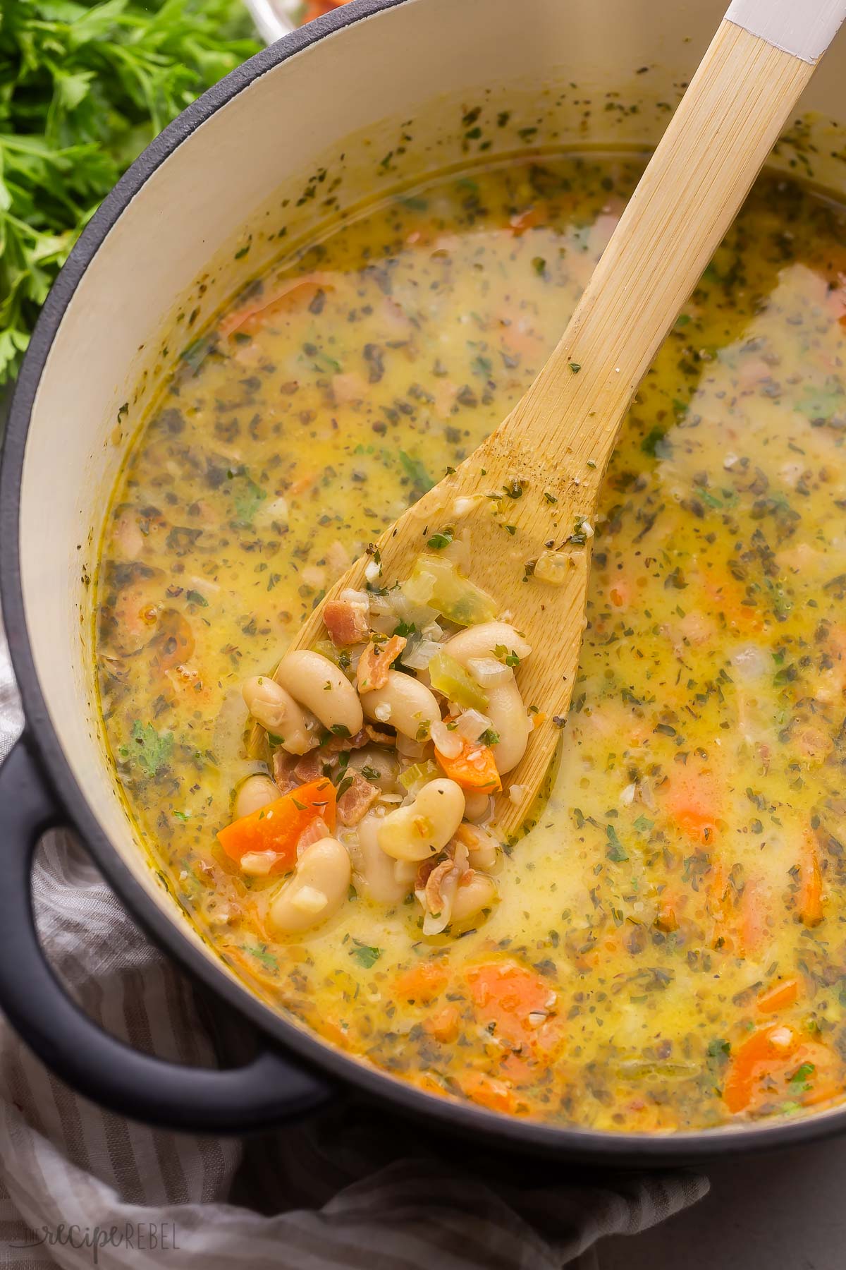 black pot of bacon white bean soup with wooden ladle in it.