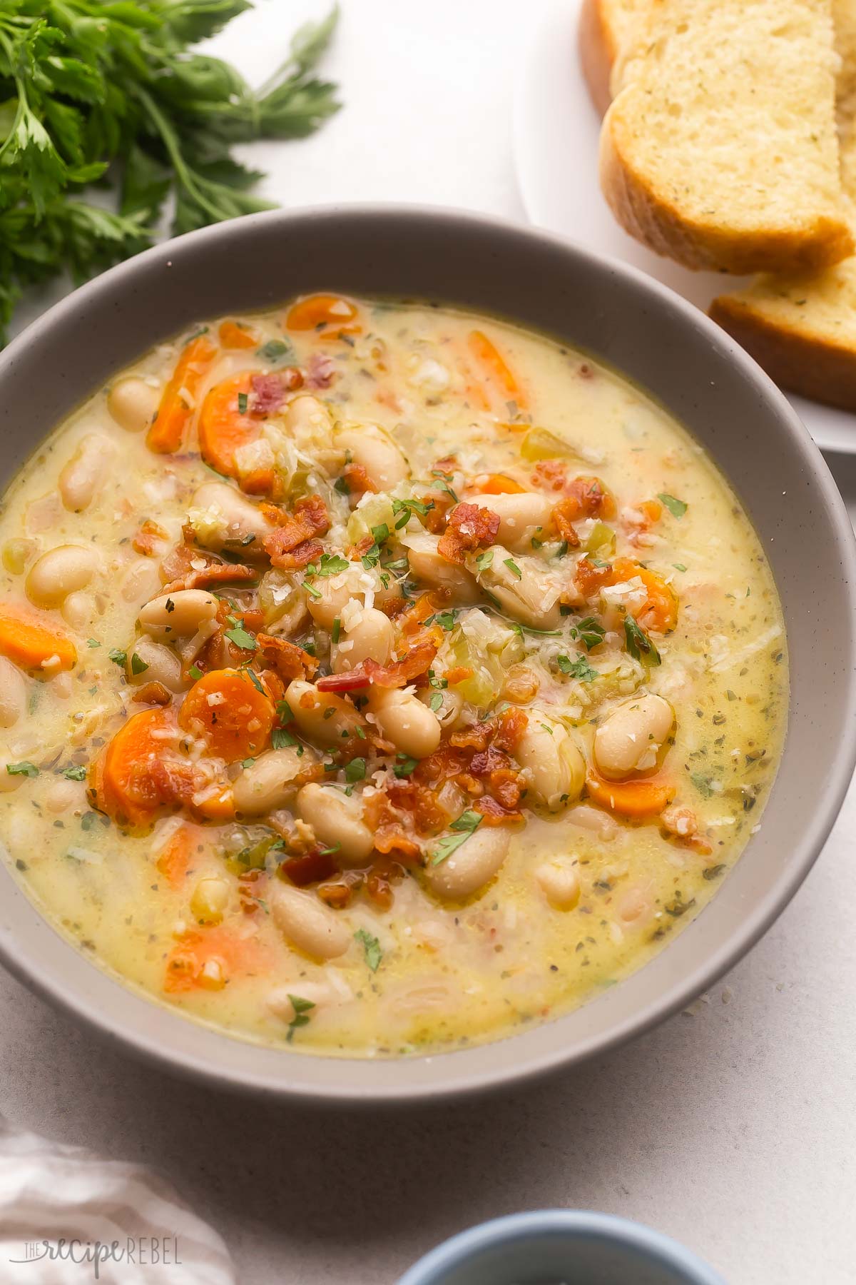 large bowl of bacon white bean soup with garlic toast and parsley beside.