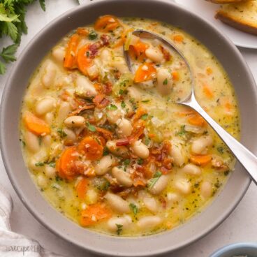 full bowl of bacon white bean soup garnished with chopped parsley.