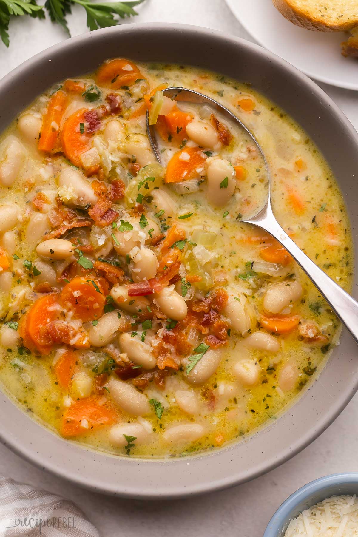 close up of a spoon in a bowl of bacon white bean soup.