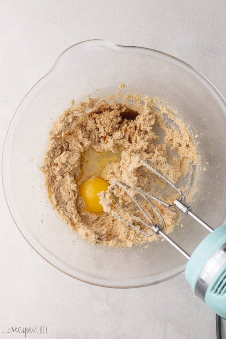 mixed ingredients in glass bowl with egg added and mixer beside.