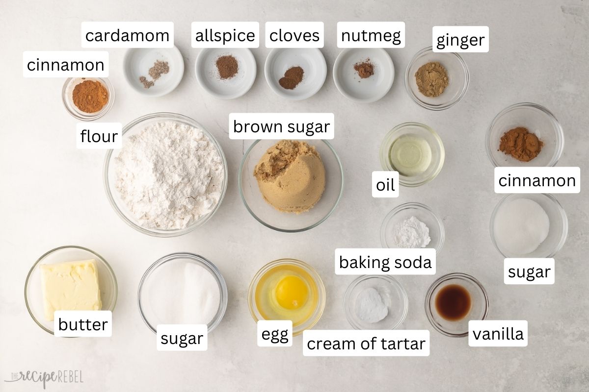 ingredients for chai cookies in glass bowls on grey surface.