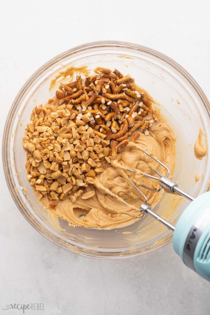 Top view of a glass mixing bowl with peanuts and pretzels on top of the creamed mixture.