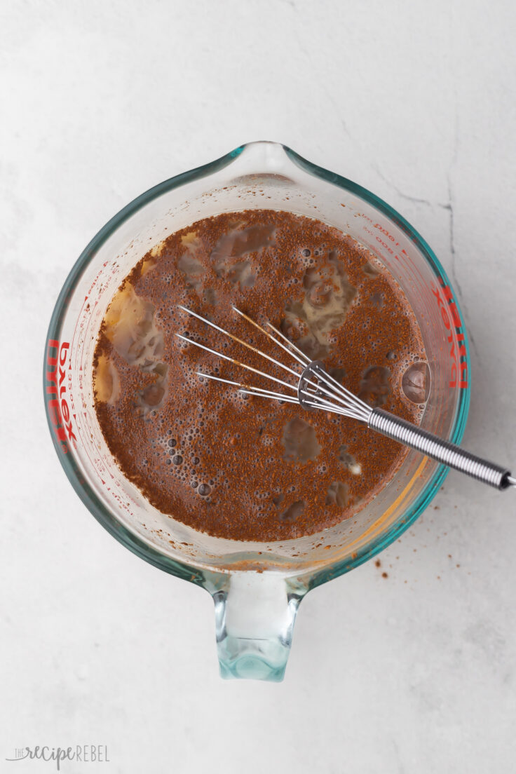 Top view of cinnamon, vanilla, maple syrup, and melted butter in a glass mixing bowl with a whisk in it.