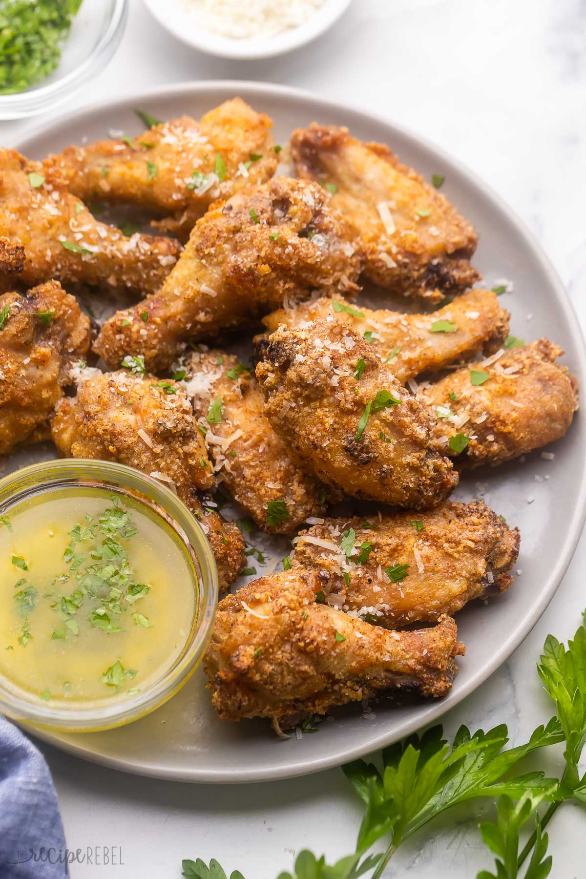 Garlic Parmesan Chicken Wings have perfectly crispy skin, flavored with Parmesan cheese, seasoning salt, garlic powder, paprika, and black pepper, all served with a homemade garlic butter sauce with parsley and extra parmesan cheese! #chicken #recipe #dinner | appetizer recipes | easy appetizer | finger foods | party food | game day food | chicken wing recipe Garlic Parmesan Chicken Wings on a white plate.