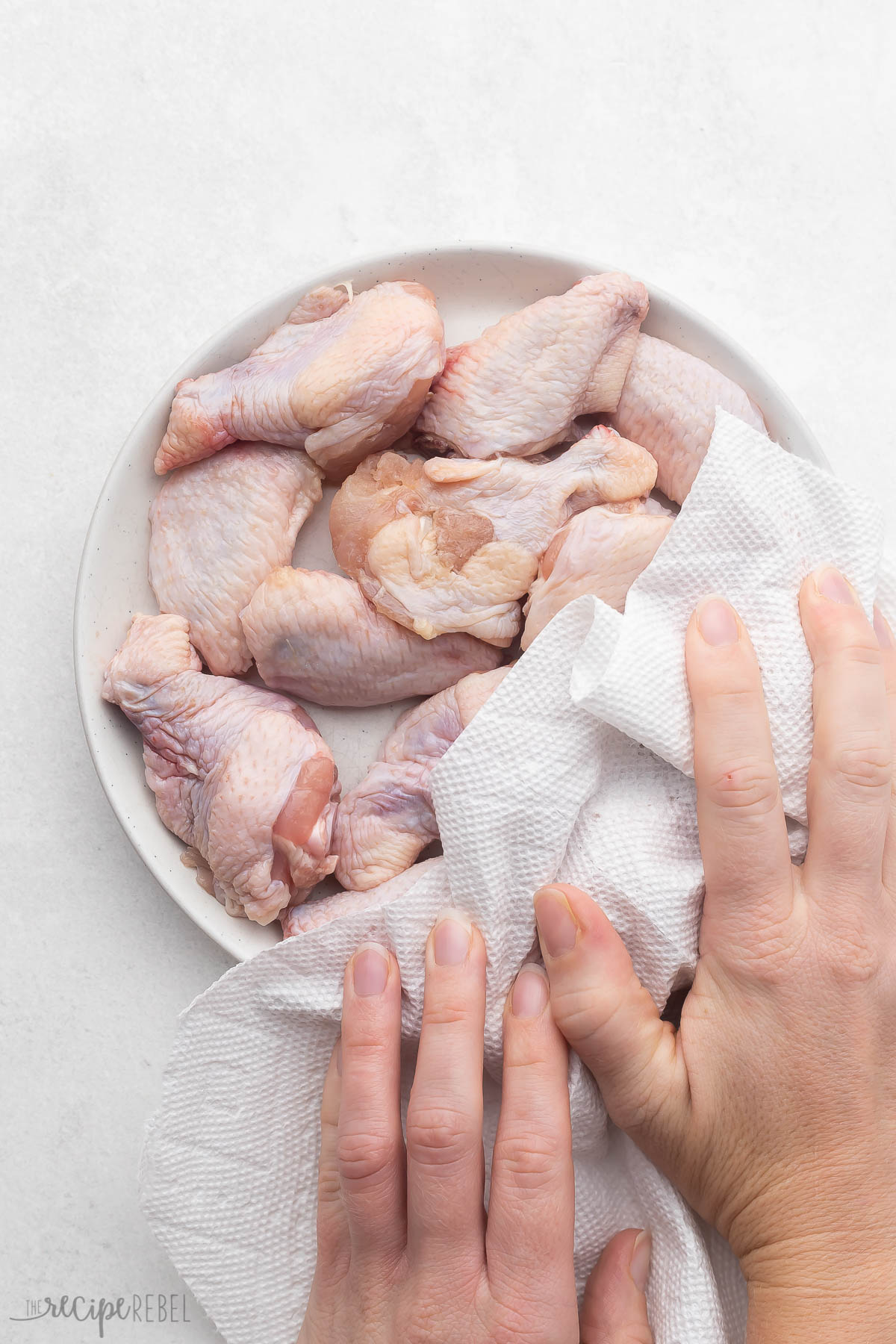 Hands patting down the raw chicken with a paper towel.