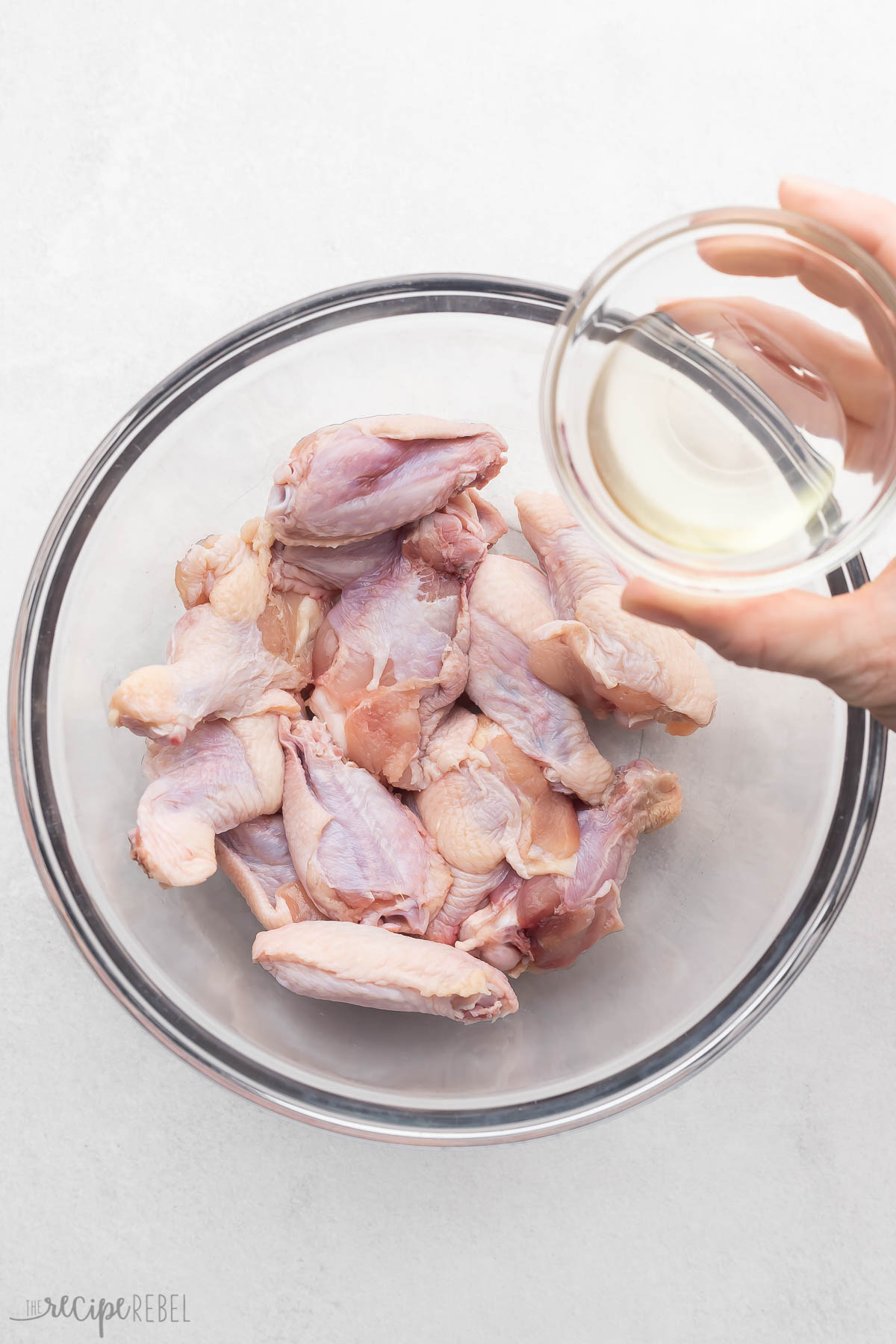 Wings in a medium bowl with oil being added in order to toss the wings.