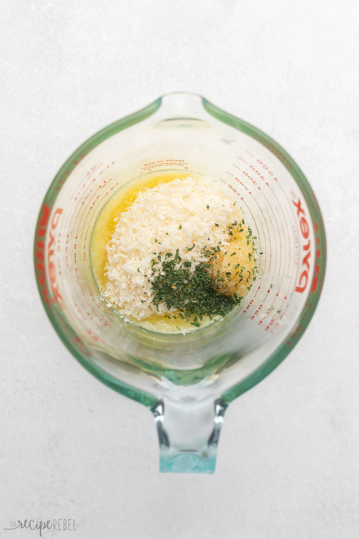 Garlic Parmesan Sauce ingredients (melted butter, parmesan, garlic, and parsley) in a glass mixing jug.