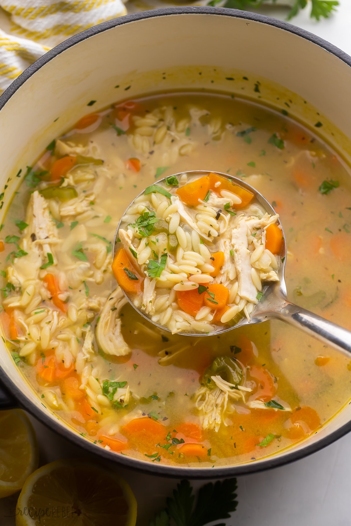 close up shot of a steel ladle filled with lemon chicken orzo soup above pot.