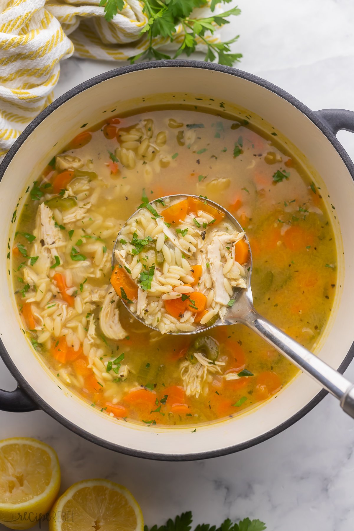 a full ladle of lemon chicken orzo soup above black and white pot full of soup.