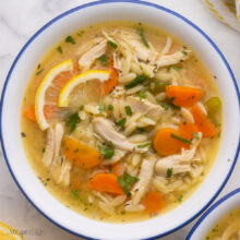 close up of a full bowl of lemon chicken orzo soup on grey surface.