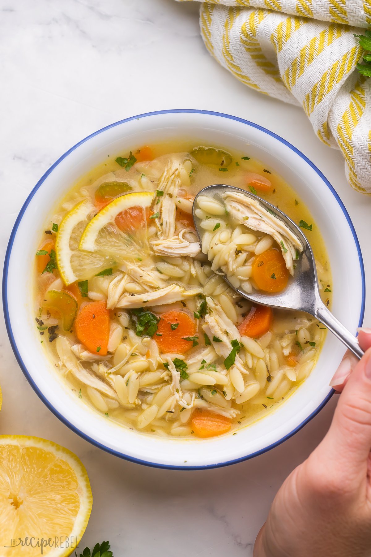 spoonful of lemon chicken orzo soup being scooped out of bowl.