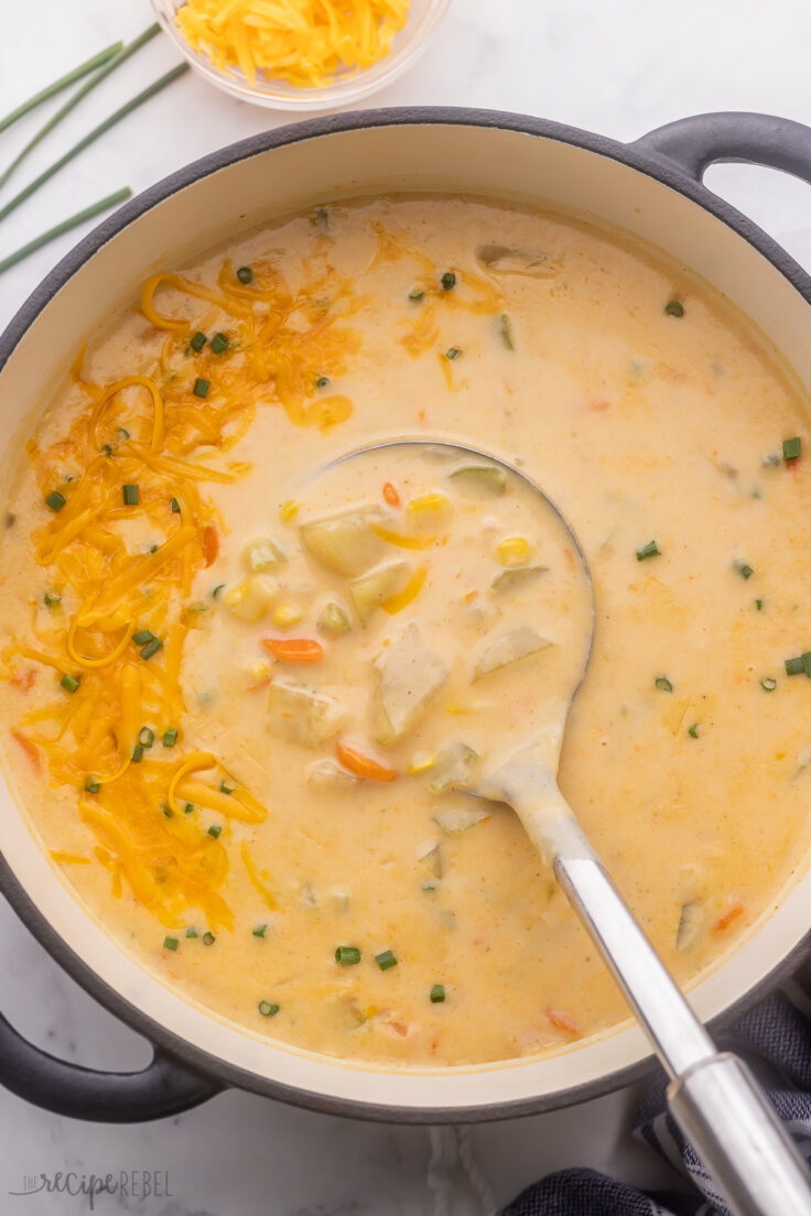 overhead view of full pot of nacho potato soup with ladle in and melted cheese on top.