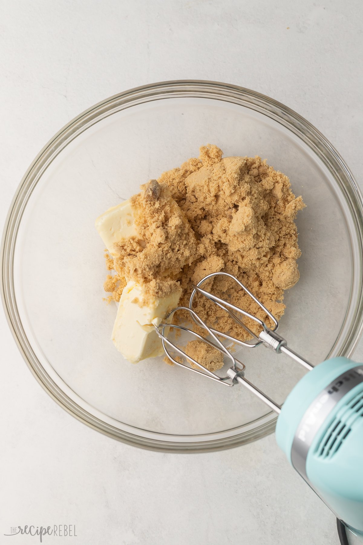 Top view of a glass mixing bowl with creamed butter and sugar in it with an electric mixer in the bowl.